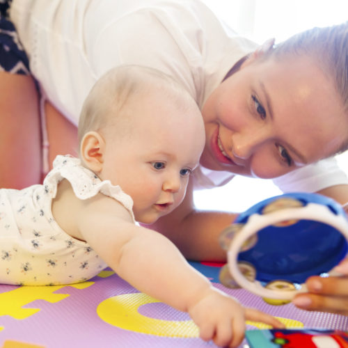 Happy and caring mother laughing together with her child. Smiling and cute young baby girl playing on mat.